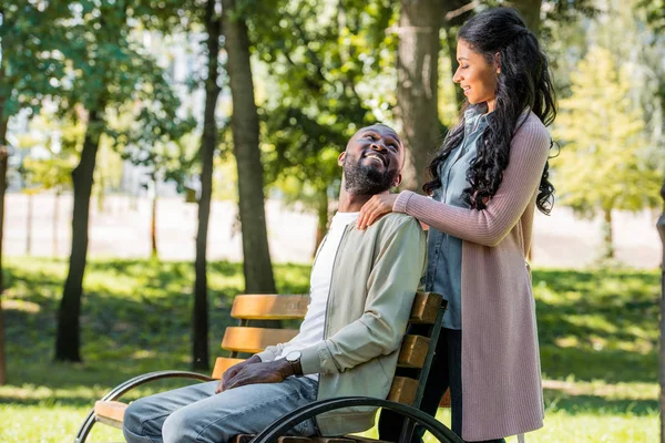 African American Girlfriend Hugging Boyfriend Back While Sitting Bench Park — стоковое фото