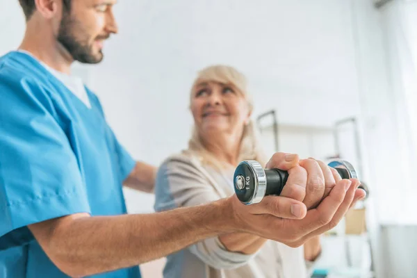 Close View Social Worker Helping Smiling Senior Woman Exercising Dumbbells — стоковое фото